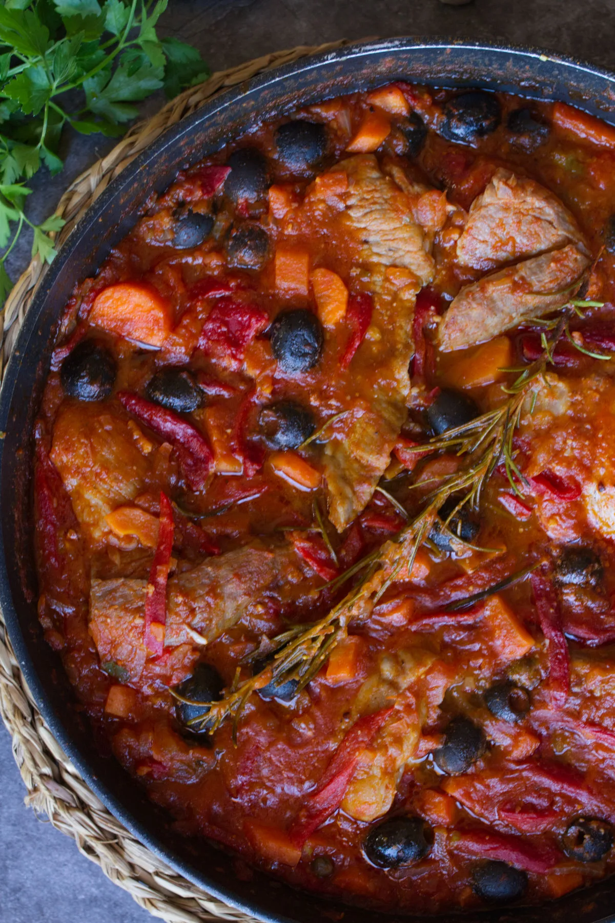 A large pan of Spanish pork secreto garnished with fresh roasemary and black olives.