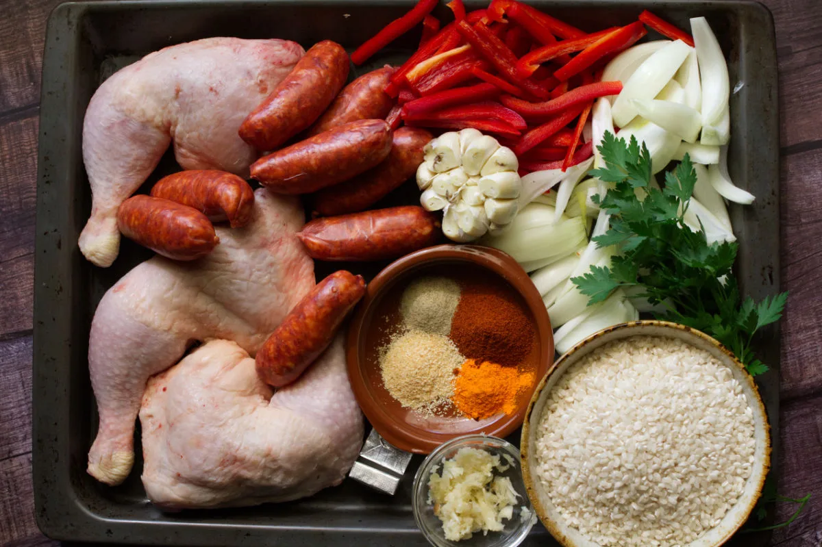 Chicken quarters, chorizo sausage, bomba rice, veggies, herbs and spices all sit in a large sheet pan.