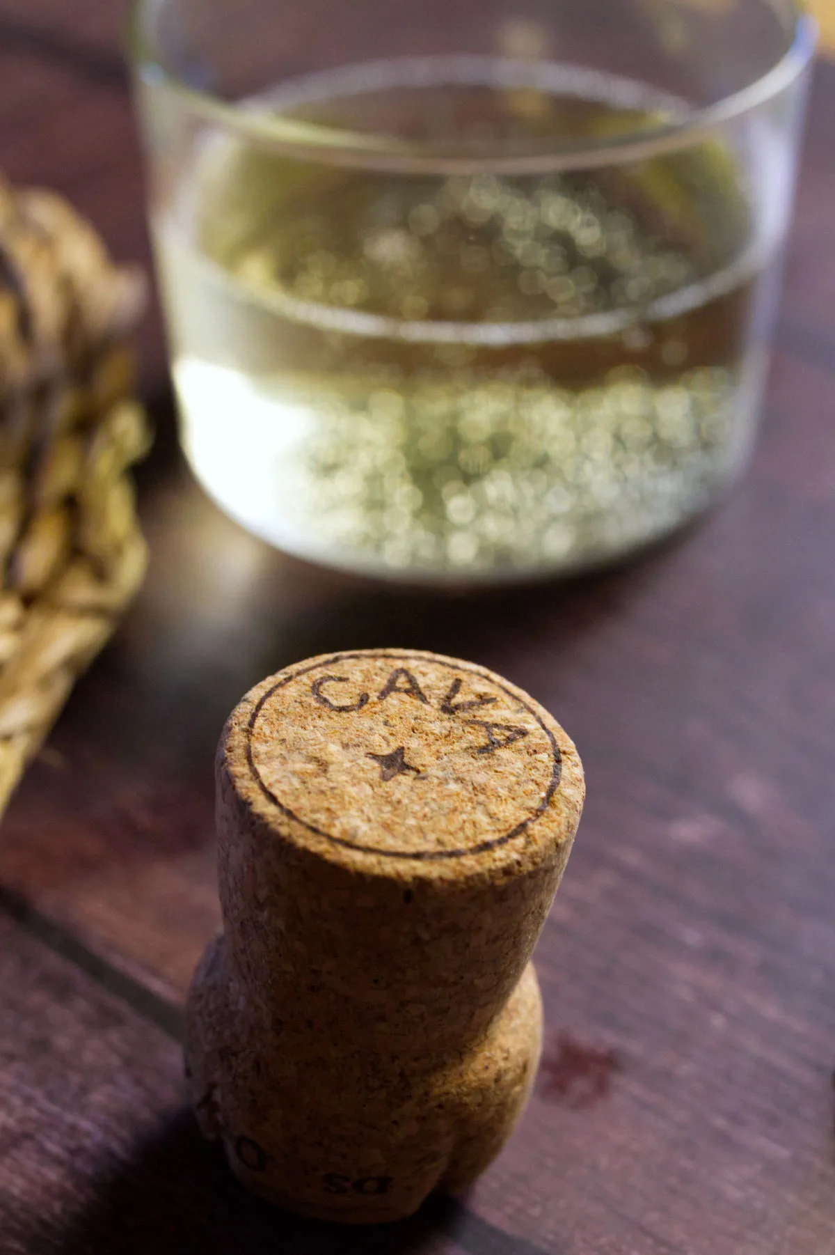 A cork from an opened bottle of Cava sits beside a glass of Cava.