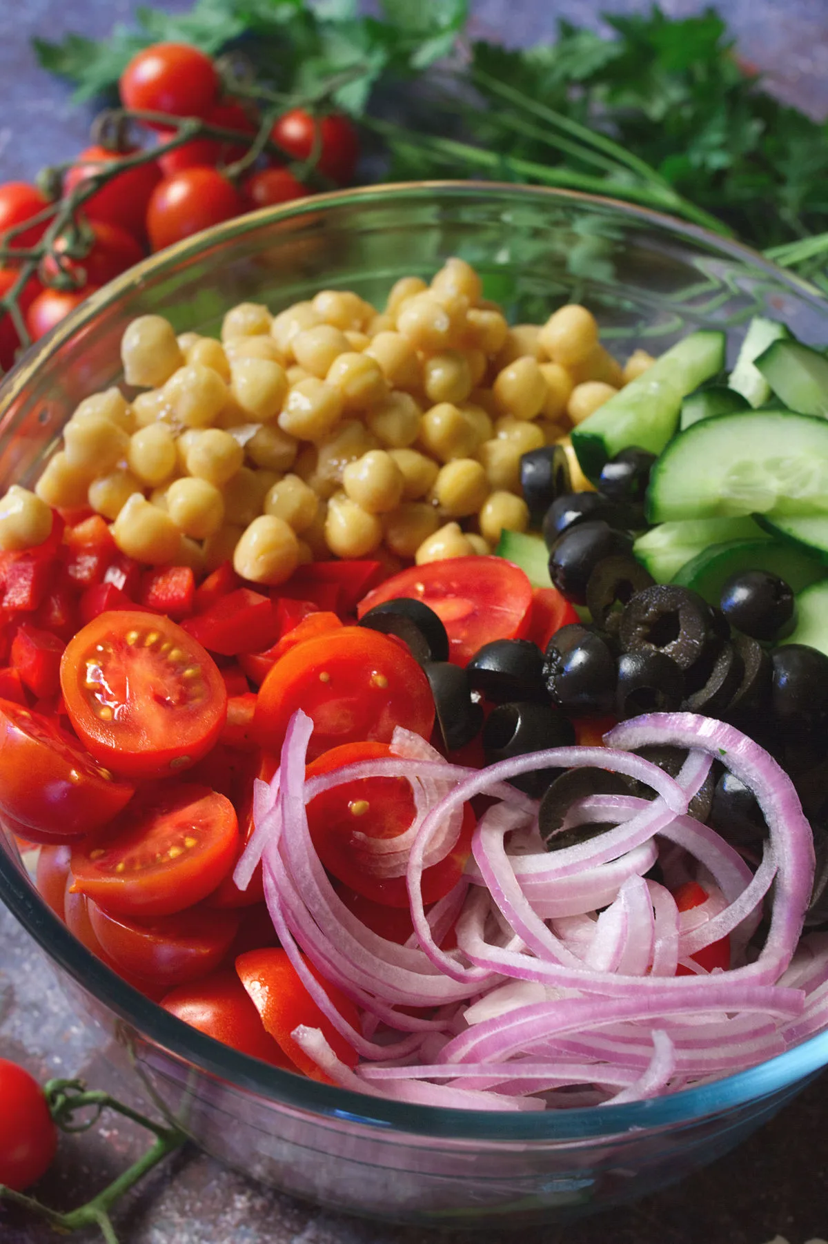ingredients for making Mediterranean chickpea salad sit unmixed in a large glass bowl. 