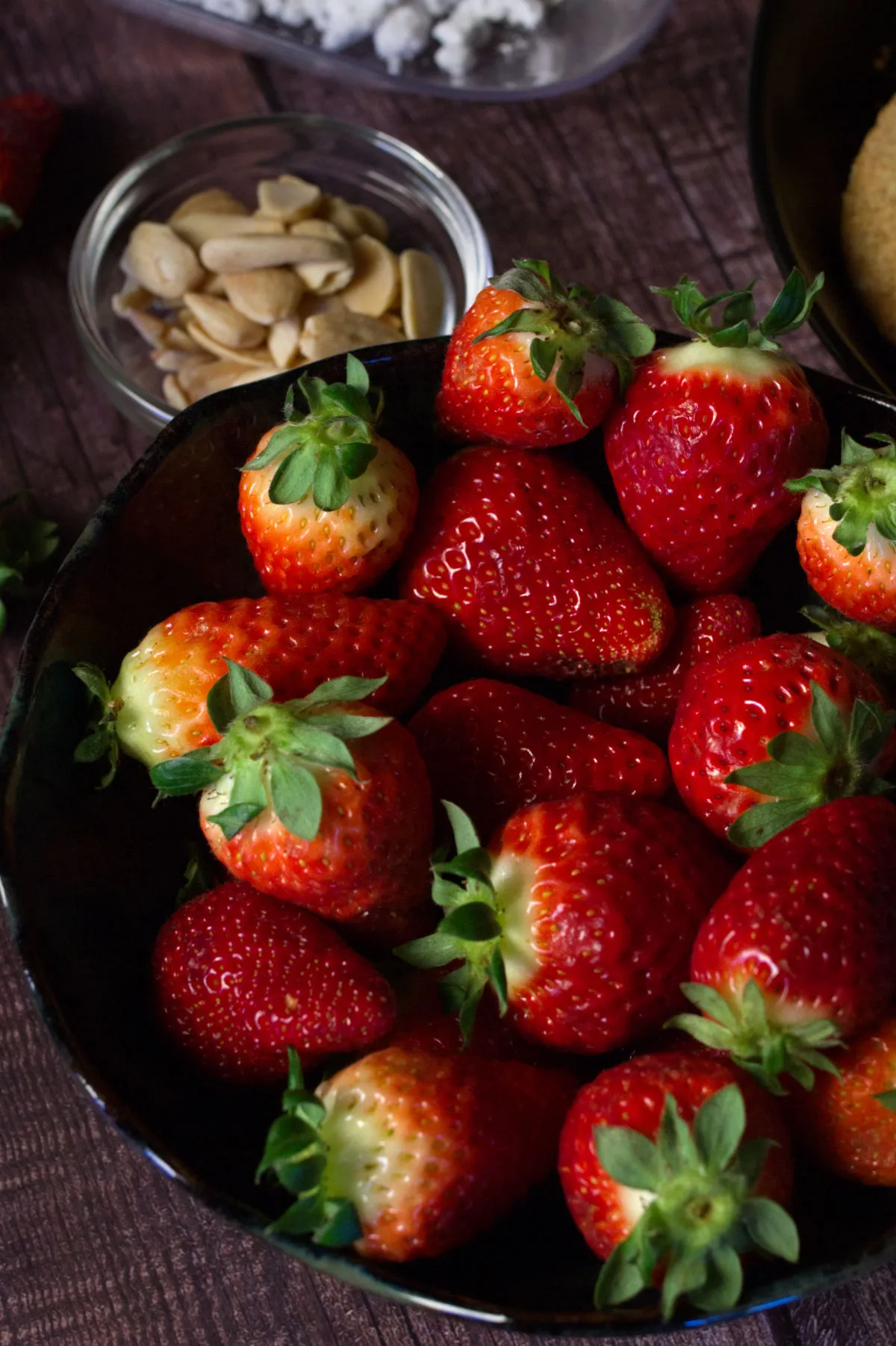 A bowl of fresh strawberries sits beside a small bowl of salted almonds.