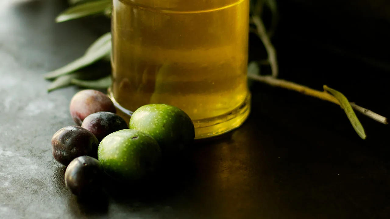 A few olives sit beside a bottle of olive oil. 
